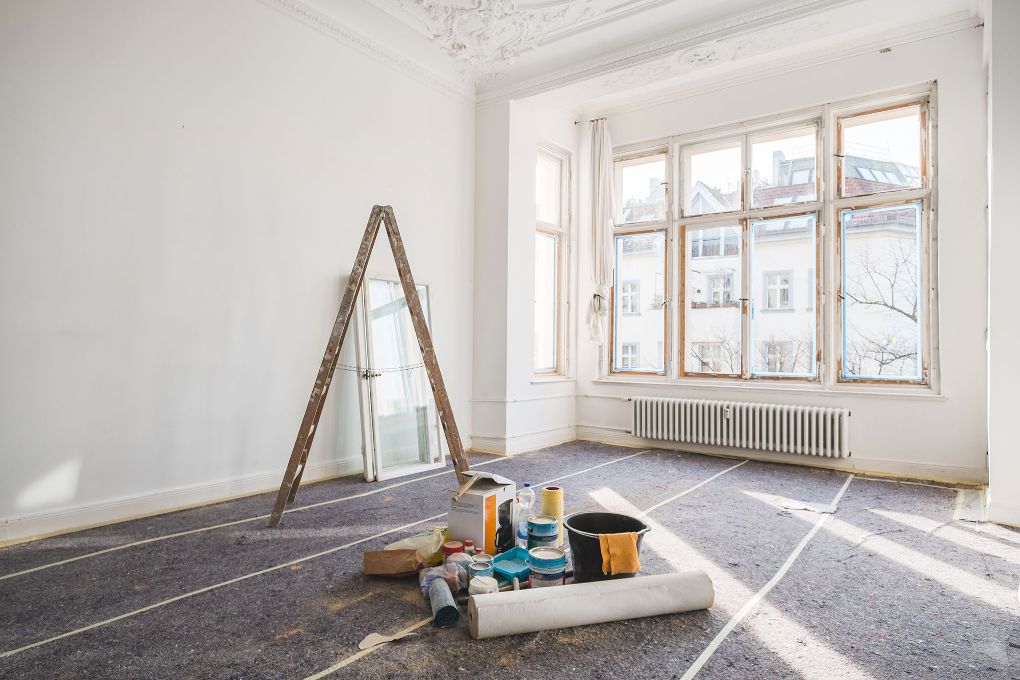 Interieur van een kamer die gerenoveerd wordt, met een trapladder en emmers verf op de voorgrond