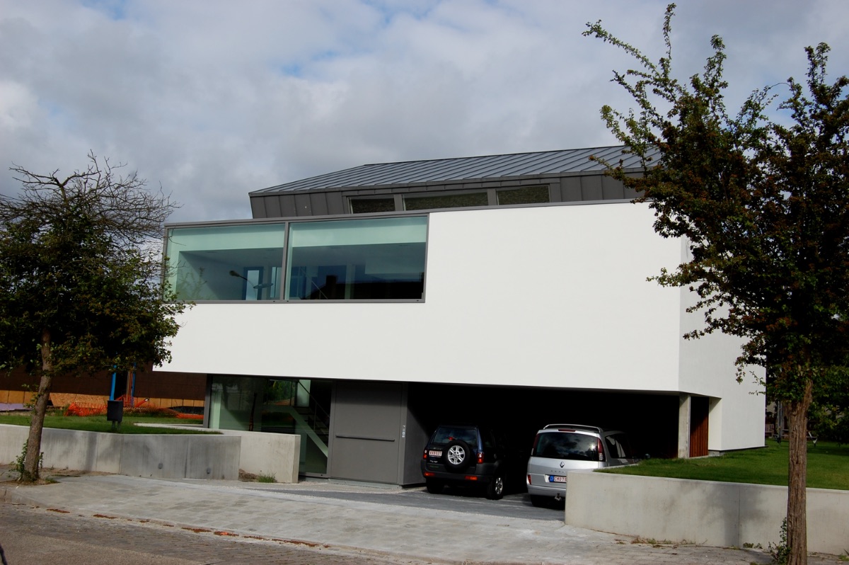 Vooraanzicht van moderne witte nieuwbouwwoning met een zwart dak, realisatie van Plan Architectenbureau Brugge