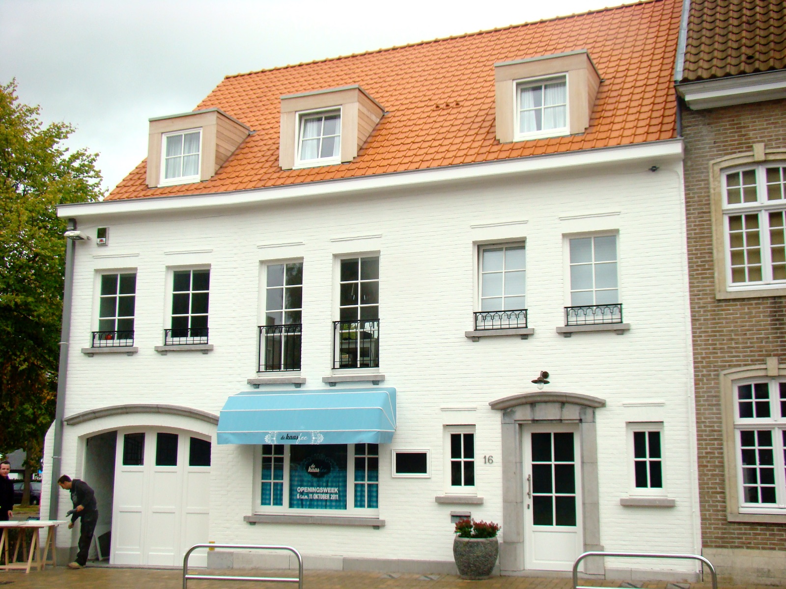 Gerenoveerde handelszaak, voorgevel van wit gebouw met twee verdiepingen en een rood dak, realisatie van Plan Architectenbureau Brugge